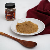Jar Rendang Nusantara Mix Rub 100 gram di samping piring berisi bubuk bumbu rendang dan sendok kayu