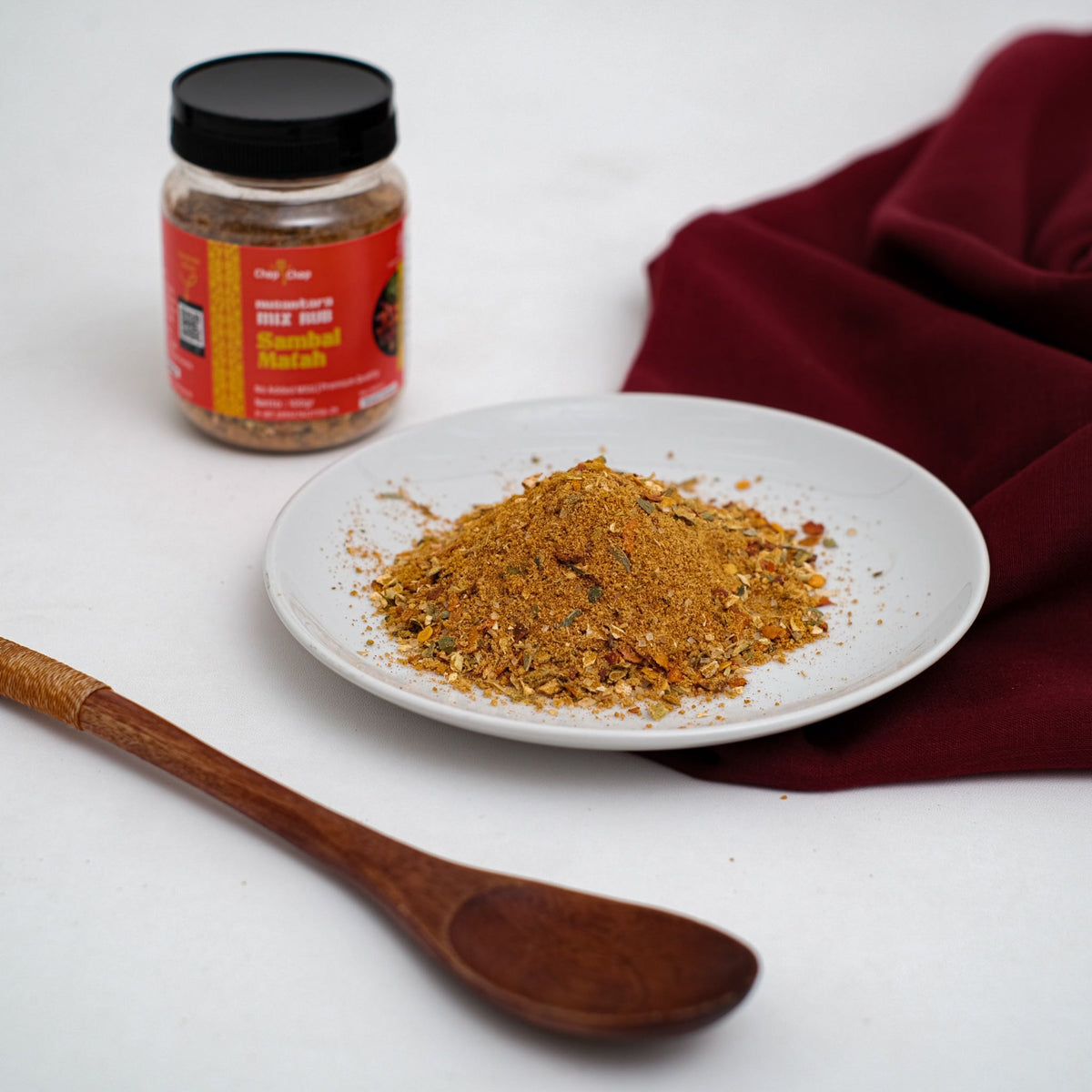 Jar Sambal Matah Nusantara Mix Rub 100 gram di samping piring berisi bubuk bumbu sambal matah dan sendok kayu