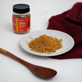 Jar Sambal Matah Nusantara Mix Rub 100 gram di samping piring berisi bubuk bumbu sambal matah dan sendok kayu