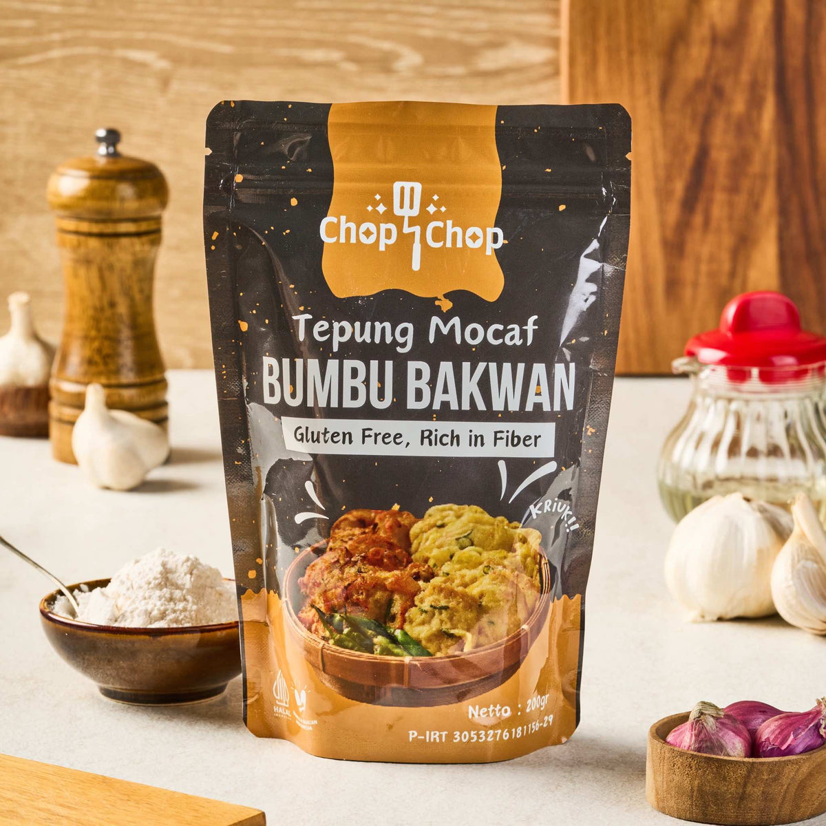 Pouch Tepung Mocaf Bumbu Bakwan 200 gram di meja dapur dengan bawang putih dan bawang merah