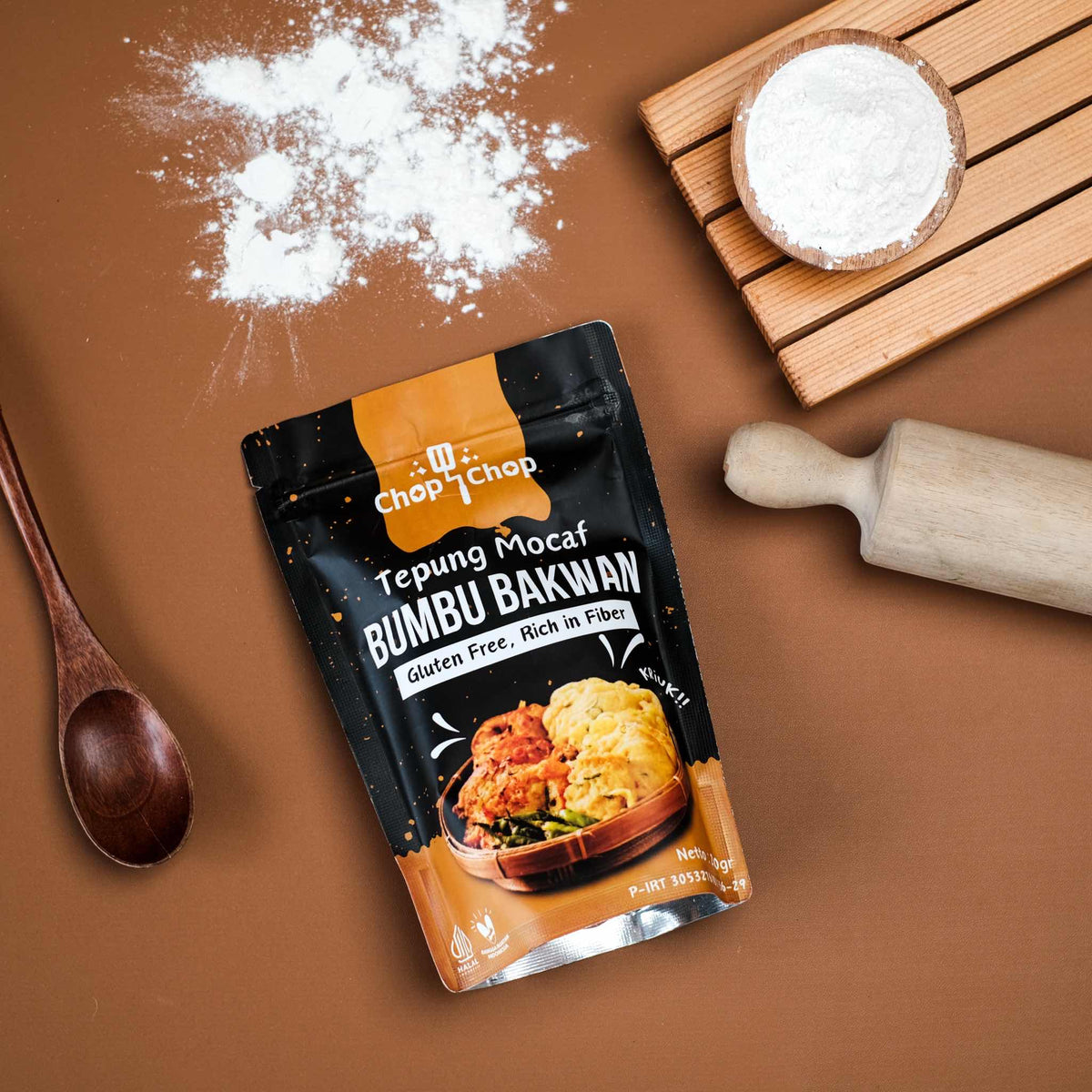 Pouch Tepung Mocaf Bumbu Bakwan dengan rolling pin, sendok kayu, dan tepung tertabur, tampak dari atas