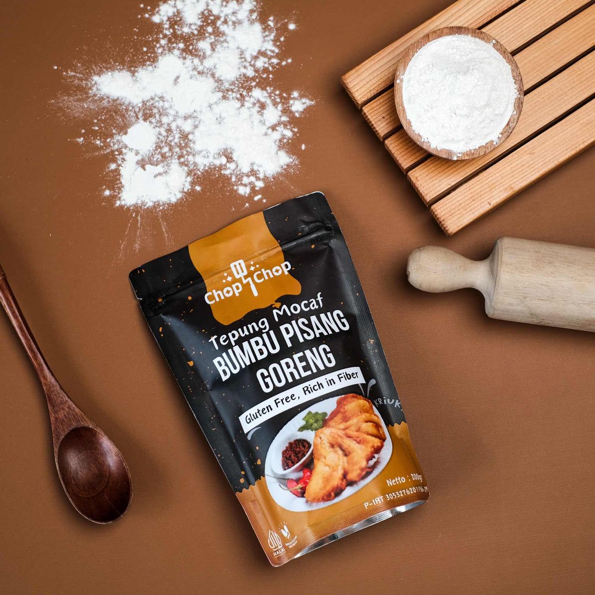 Pouch Tepung Mocaf Bumbu Pisang Goreng dengan rolling pin, sendok kayu, dan tepung tertabur, tampak dari atas